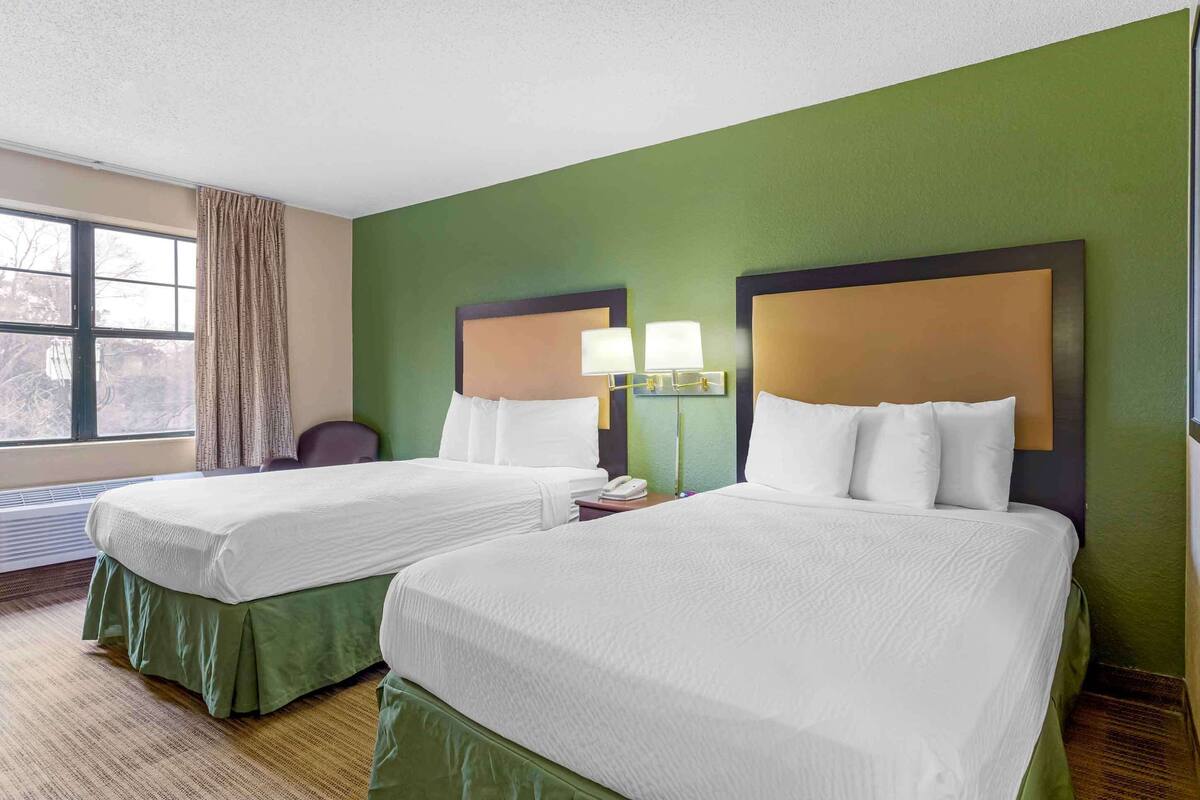 Een hotelkamer met twee bedden, groene muren en een raam met gordijnen.