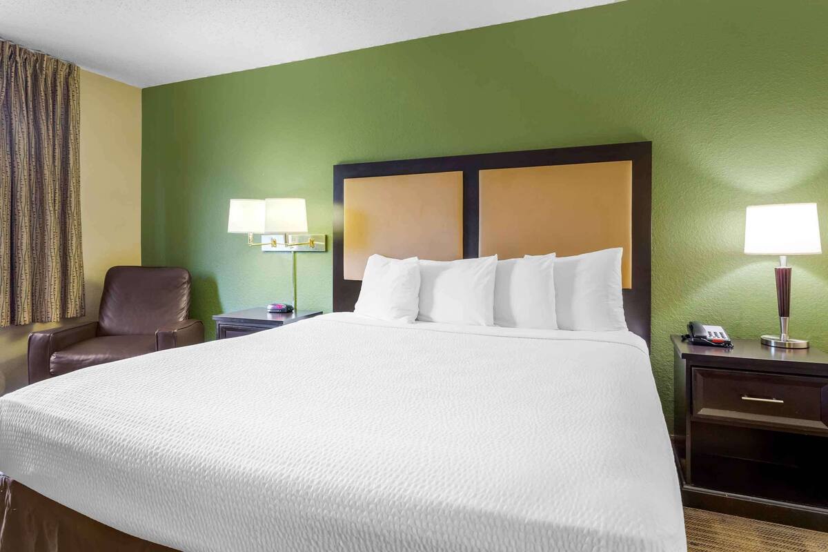 Een hotelkamer met een groot bed, twee nachtkastjes met lampen, een stoel en een groene wand.