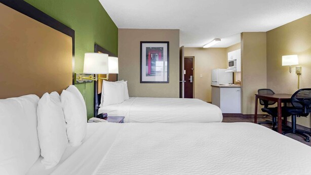 Une chambre d’hôtel avec deux lits, un bureau avec une chaise, un four à micro-ondes et une petite kitchenette.