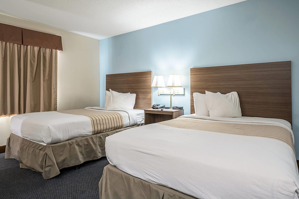 A hotel room with two beds, a nightstand, and a lamp.