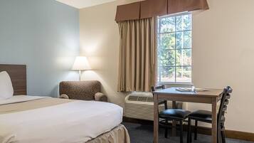 A hotel room with a bed, a chair, a desk, and a window with curtains.