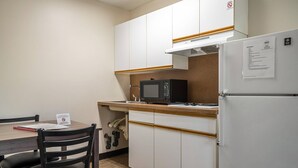 A compact kitchenette with a microwave, stove, and refrigerator. There is a small dining table with chairs and a sign indicating the room is reserved for non-smoking guests. - Suburban Studios of Wilmington (Wilmington)