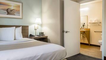 Quarto de hotel com cama, mesa de cabeceira, abajur e um quadro na parede.
