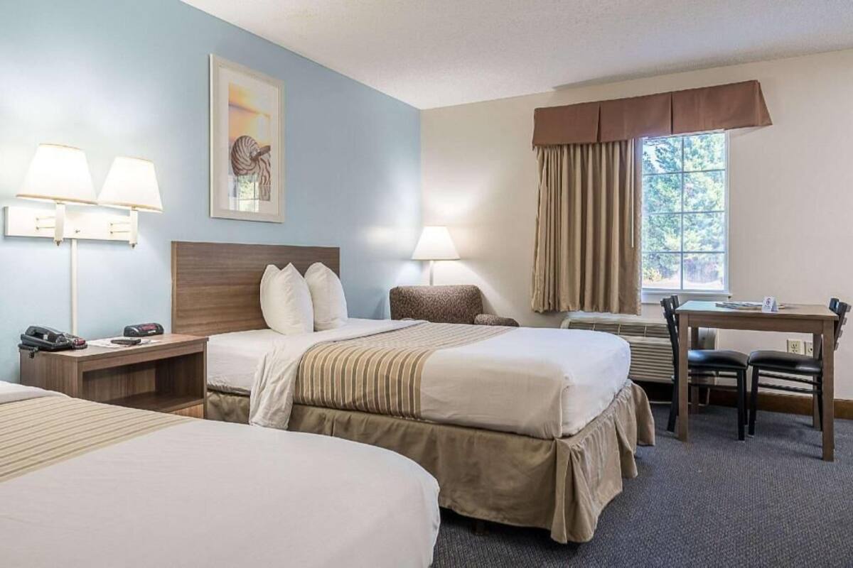 A hotel room with two beds, a desk, a chair, a telephone, and a window with curtains.
