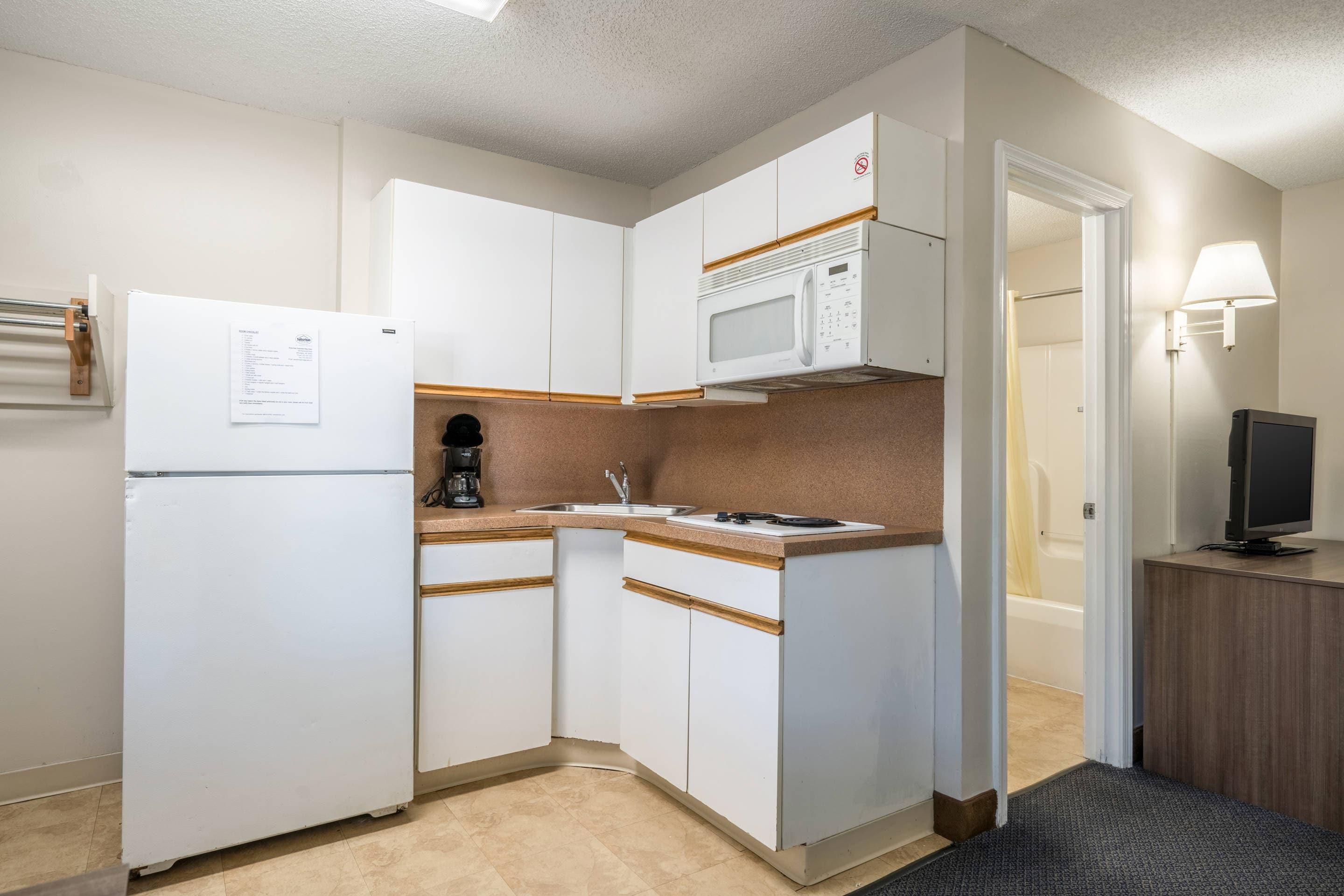 Una cocina compacta con armarios blancos, microondas, refrigerador y cafetera.