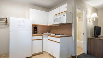 Una cocina compacta con armarios blancos, microondas, refrigerador y cafetera.