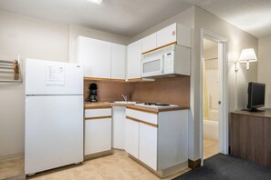 A compact kitchen with white cabinets, a microwave, a refrigerator, and a coffee maker. - Suburban Studios of Wilmington (Wilmington)