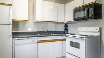 Una cocina con gabinetes blancos, un microondas negro, una estufa blanca y un lavavajillas.