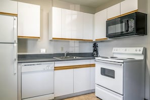 A kitchen with white cabinets, a black microwave, a white stove, and a dishwasher. - Suburban Studios of Wilmington (Wilmington)