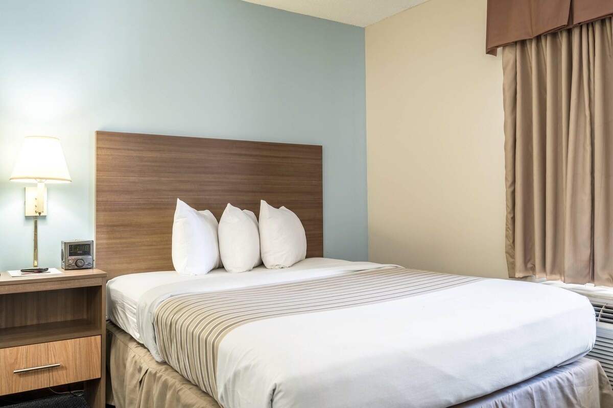 A hotel room with a wooden headboard, a bedside table with a lamp, a radio, and a bed with white bedding and striped pillows.