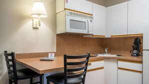 A compact kitchenette with a microwave, a coffee maker, and a sink. There are two chairs and a table. - Suburban Studios of Wilmington (Wilmington)