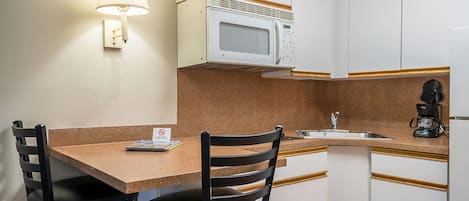 Una kitchenette compacta con microondas, cafetera y lavamanos. Hay dos sillas y una mesa.