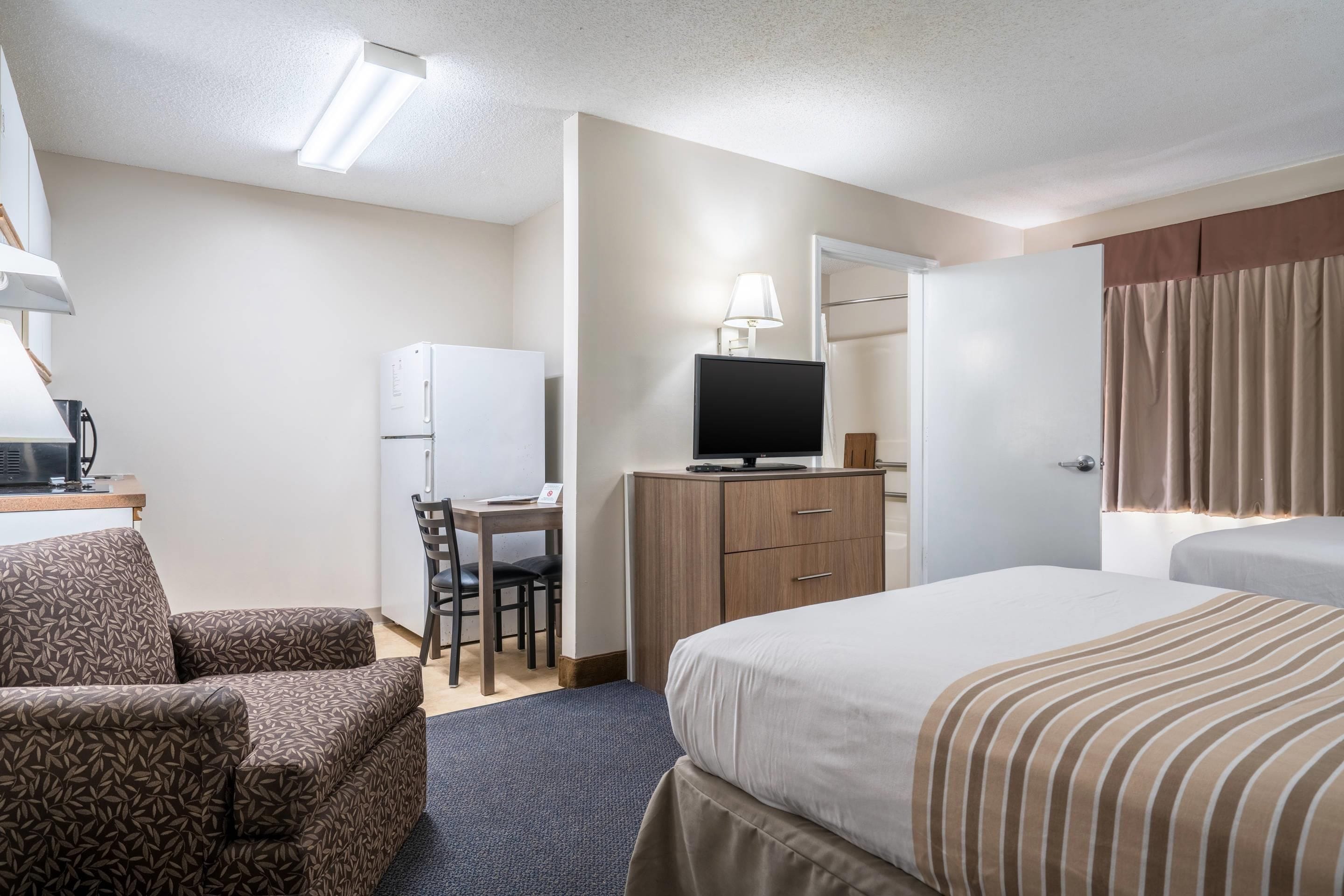 Una habitación de hotel con cama, escritorio con computadora, televisor, armario y una silla.