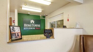 Un mostrador de recepción con una pared verde, un cartel enmarcado para Home Towne Studios by RedRoof y una cafetera a 24,95 dólares.