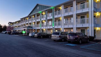 A multi-story motel with a central entrance, parking lot, and several vehicles parked in front.