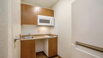 A compact kitchen with wooden cabinets, a built-in microwave, a sink, and a refrigerator.