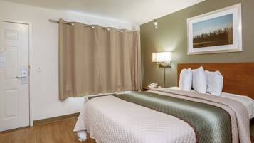 Quarto de hotel com uma cama, mesa de cabeceira, telefone, abajur, porta e um quadro pendurado na parede.
