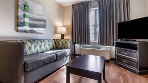 A modern hotel room with a sofa, a flat-screen TV, a table, and a painting of a lighthouse. - Extended Stay America Premier Suites Charlotte Pineville Mat (Charlotte)