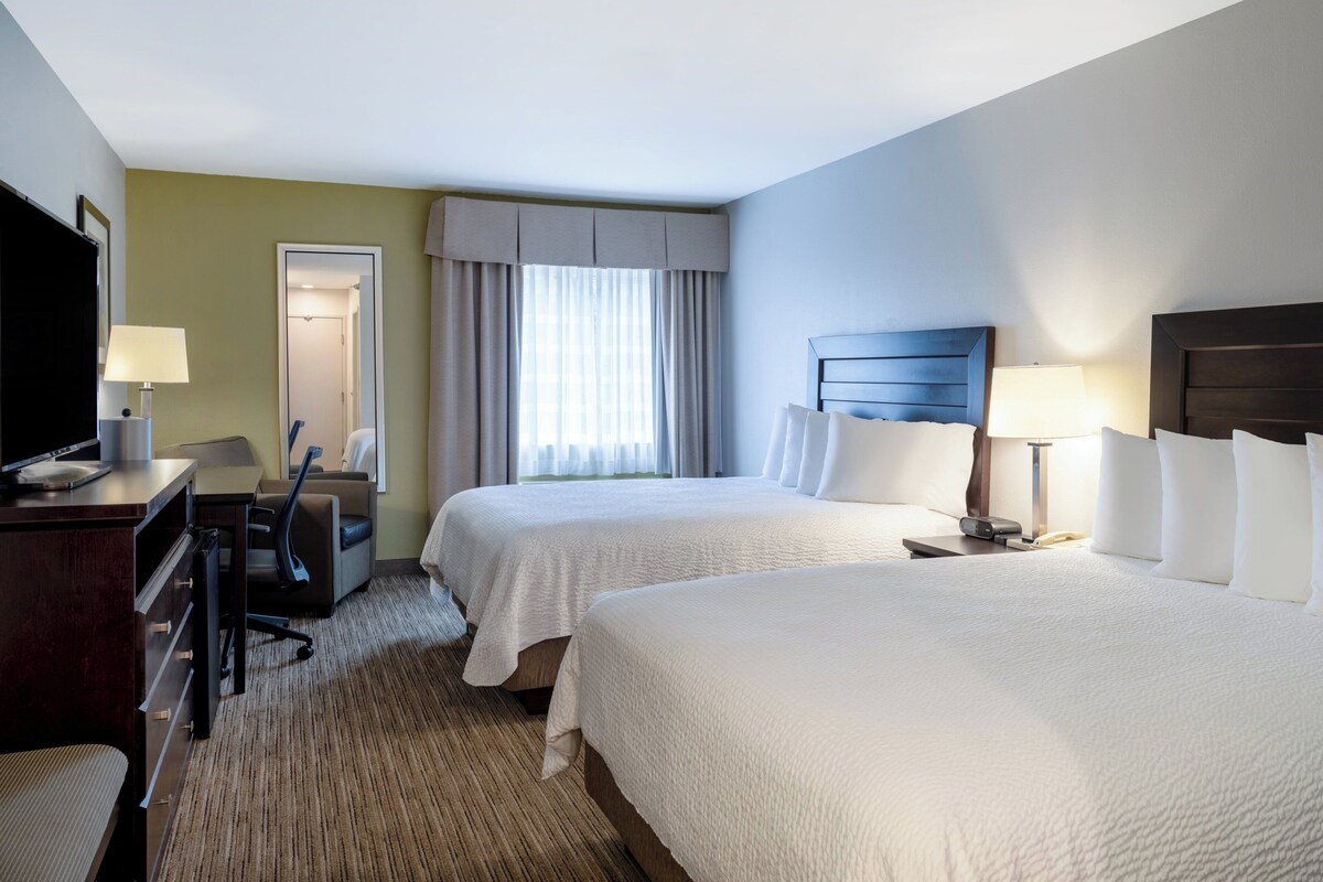 A hotel room with two beds, a desk, a chair, a TV, and a window with curtains.