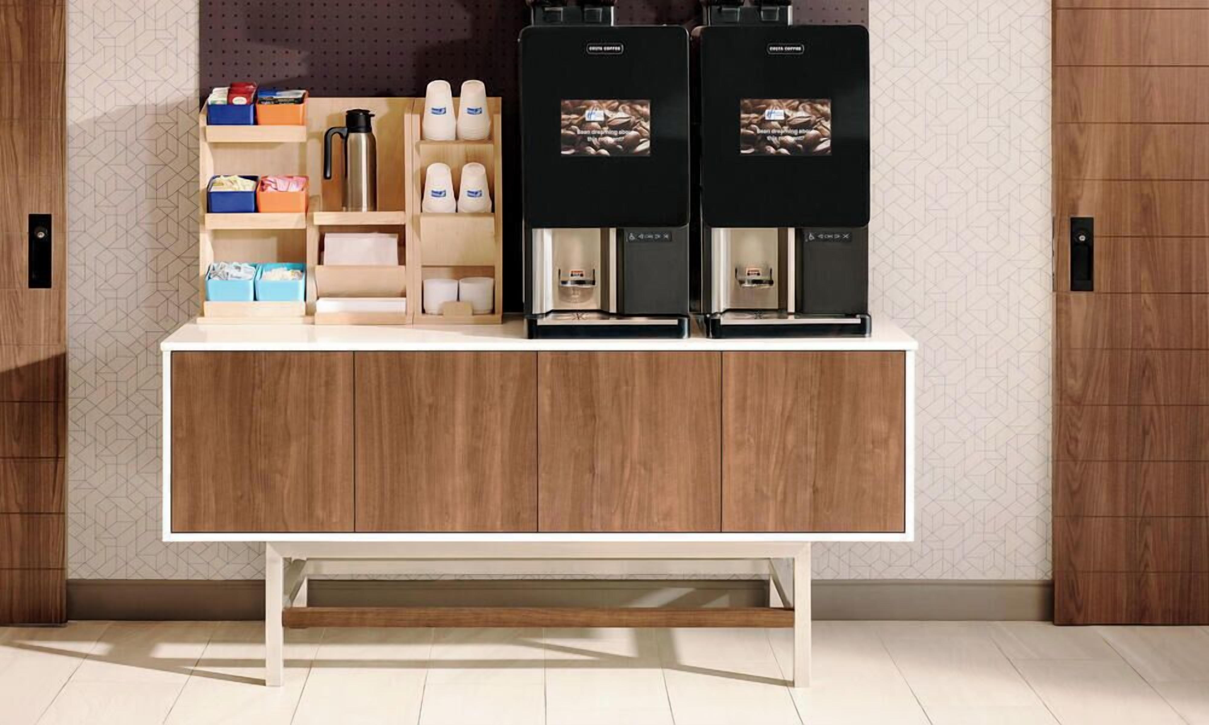 A coffee station with two espresso machines, a coffee grinder, and various coffee-related items on shelves.