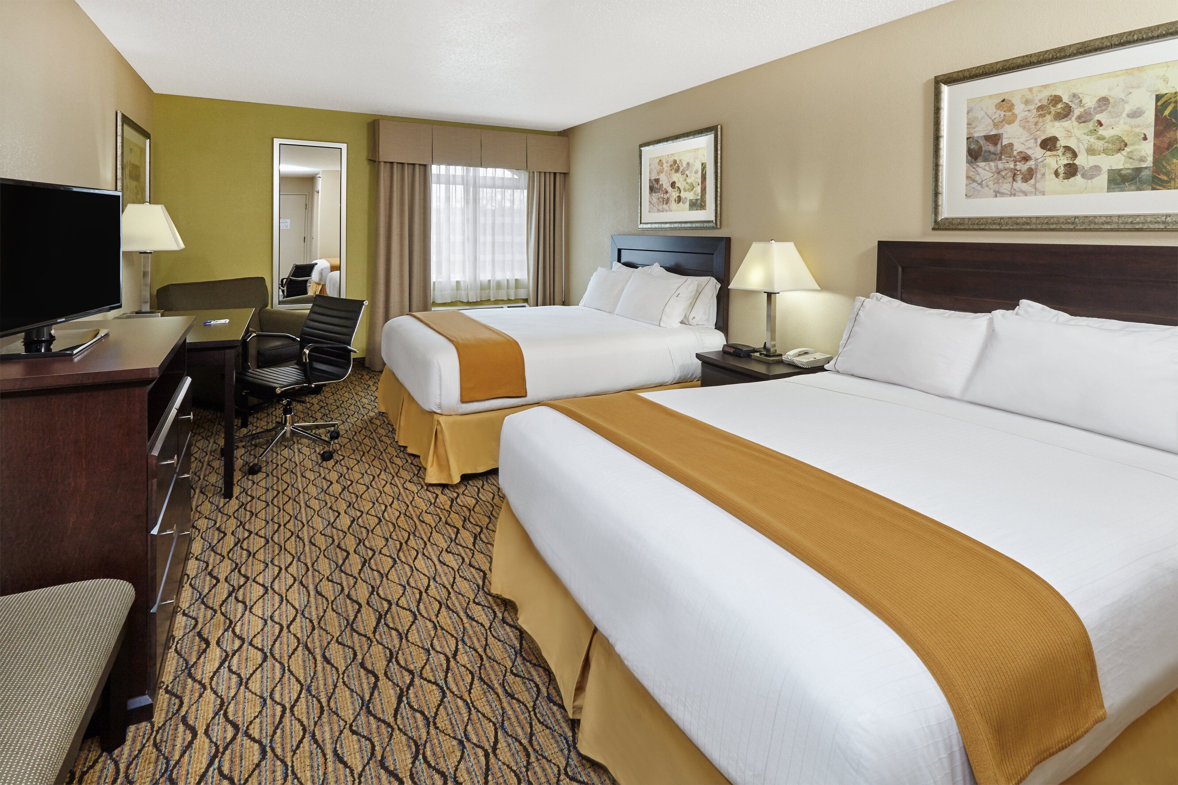 A hotel room with two beds, a desk with a television, a chair, and a patterned carpet.