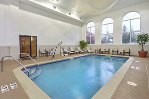 Una piscina interior con superficie de agua cristalina, rodeada de sillones de descanso y una planta en maceta.