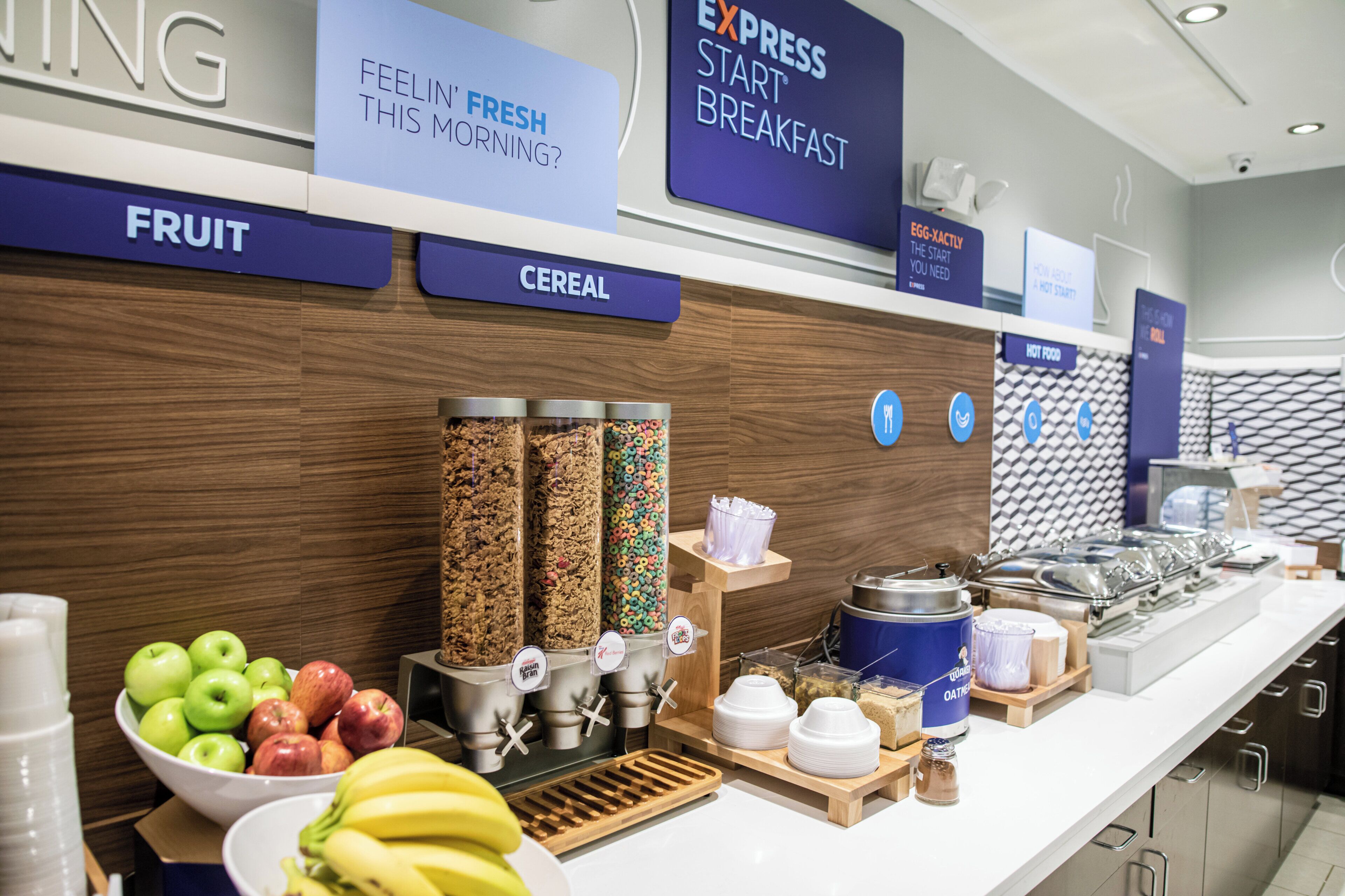 Un bufé de desayuno con secciones identificadas para fruta, cereales y comida caliente.