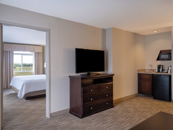 A hotel room with a bed, a TV on a wooden dresser, a kitchenette, and a view of the outdoors.