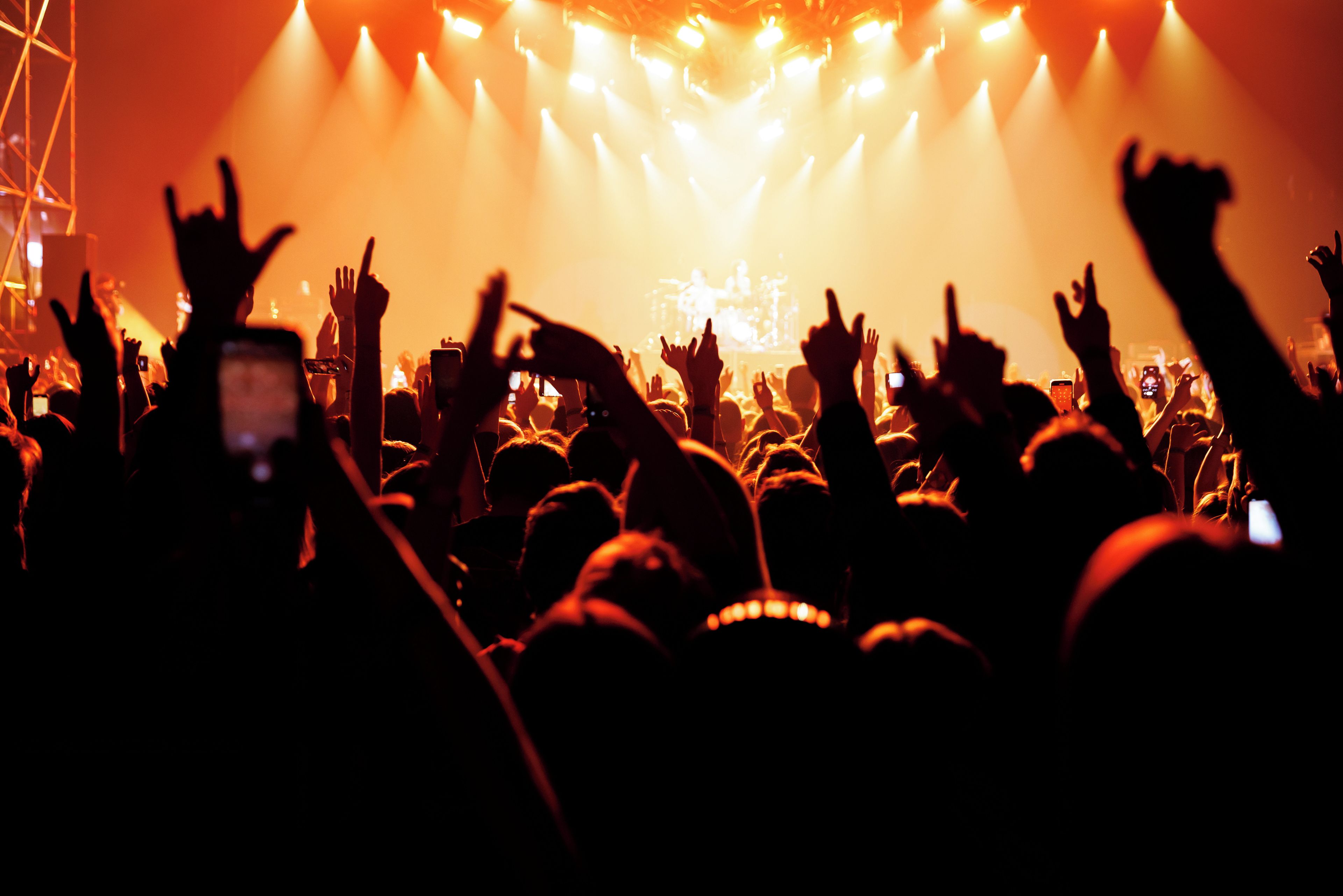 A crowd at a concert with raised hands and stage lights.
