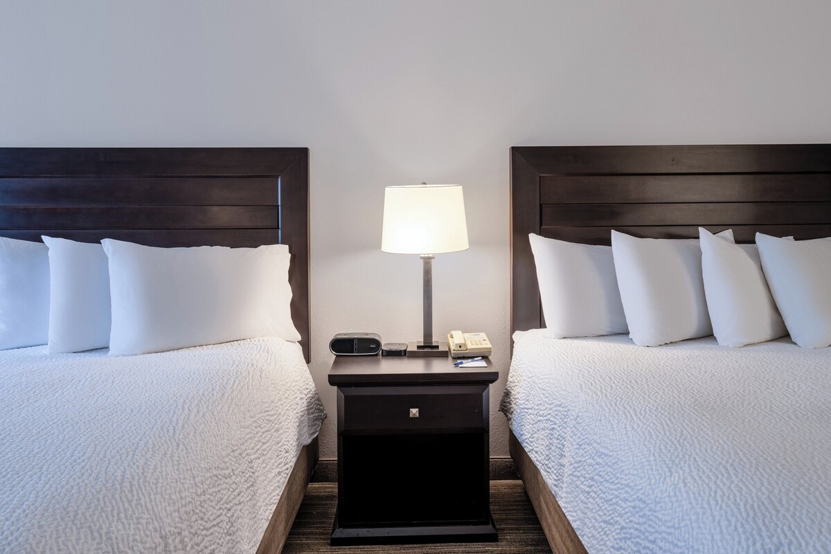 A hotel room with two beds, a nightstand with a lamp, and a phone.