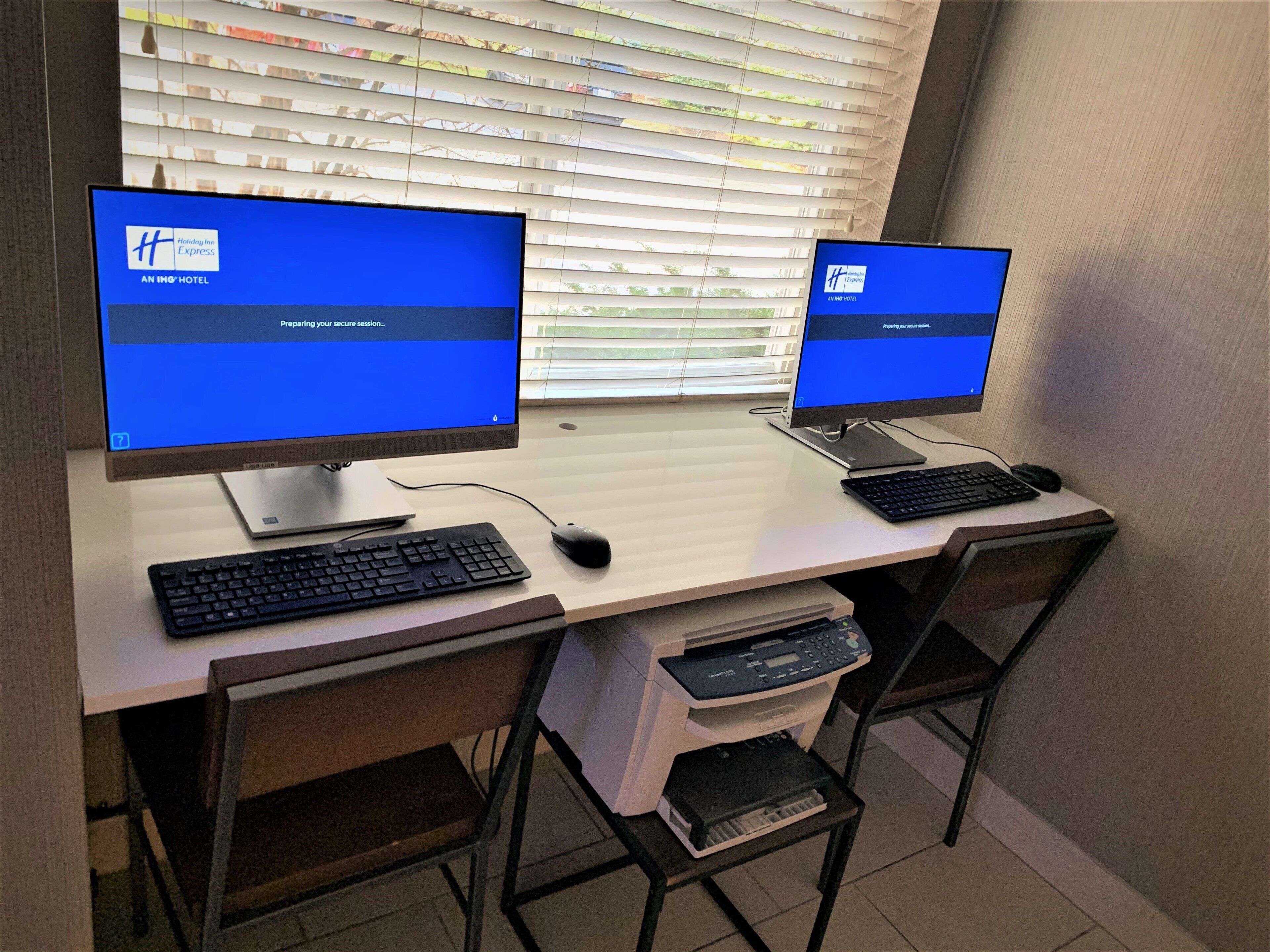 Two computer monitors on a desk with a keyboard, mouse, and printer.