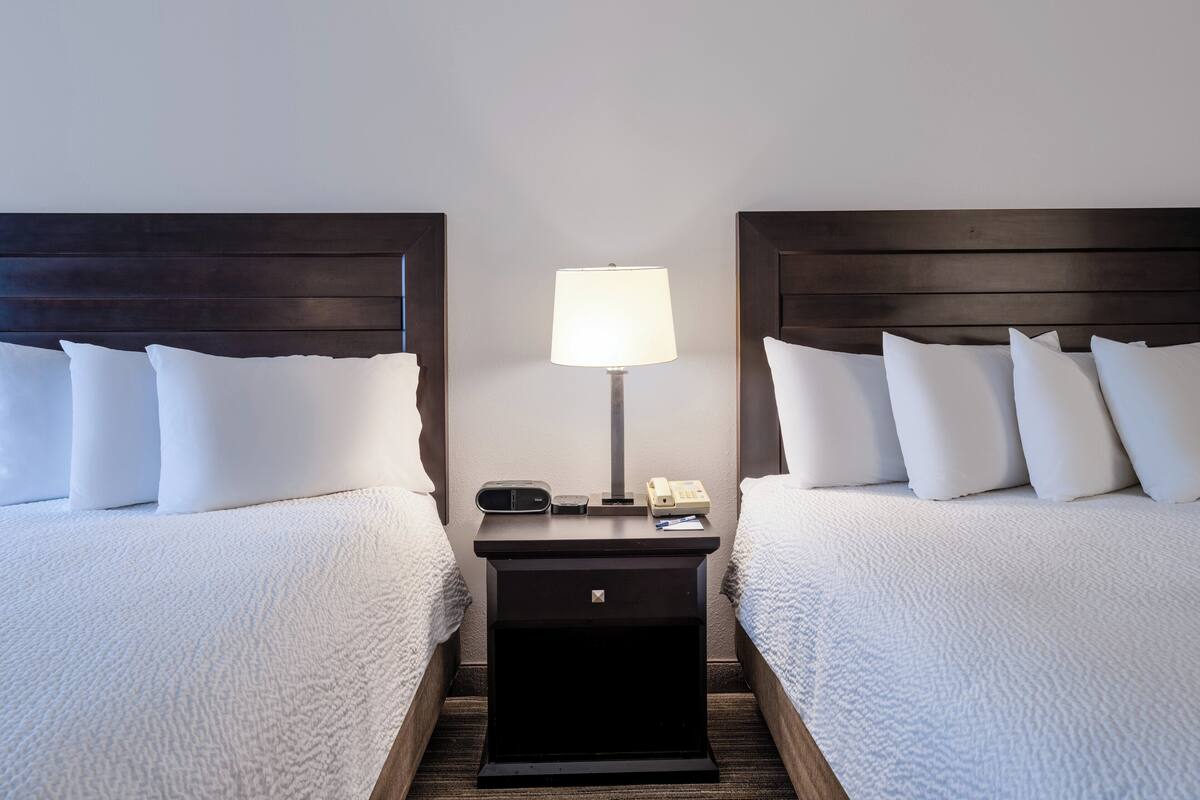 A hotel room with two beds, a nightstand with a lamp, and a phone.