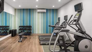 Un gimnasio con cintas de correr, mancuernas y un banco.