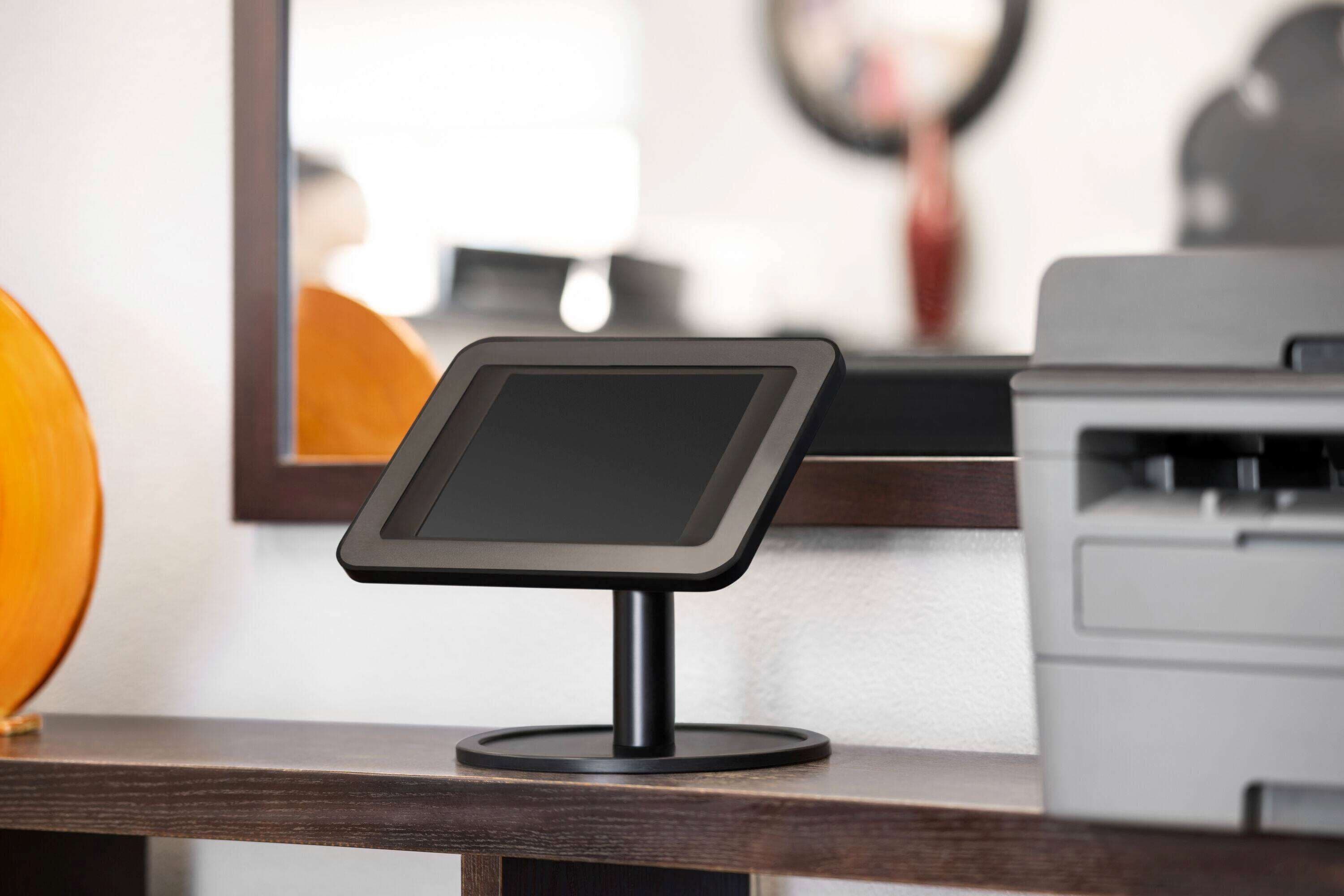 A digital kiosk on a wooden counter with a printer and a mirror in the background.