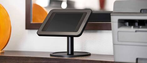 A digital kiosk on a wooden counter with a printer and a mirror in the background.