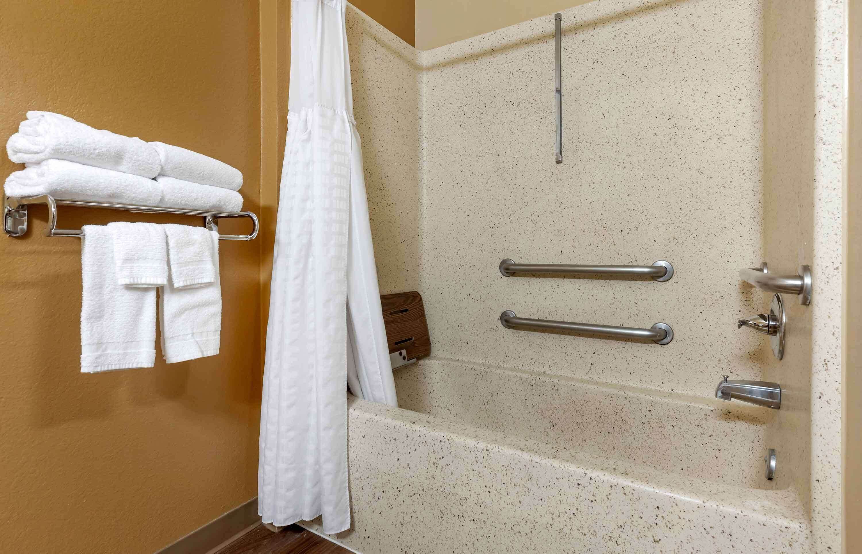 A bathroom with a bathtub, grab bars, and a towel rack with towels.