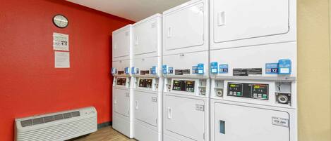 A laundry room with multiple white dryers, a clock, and a notice on the wall.