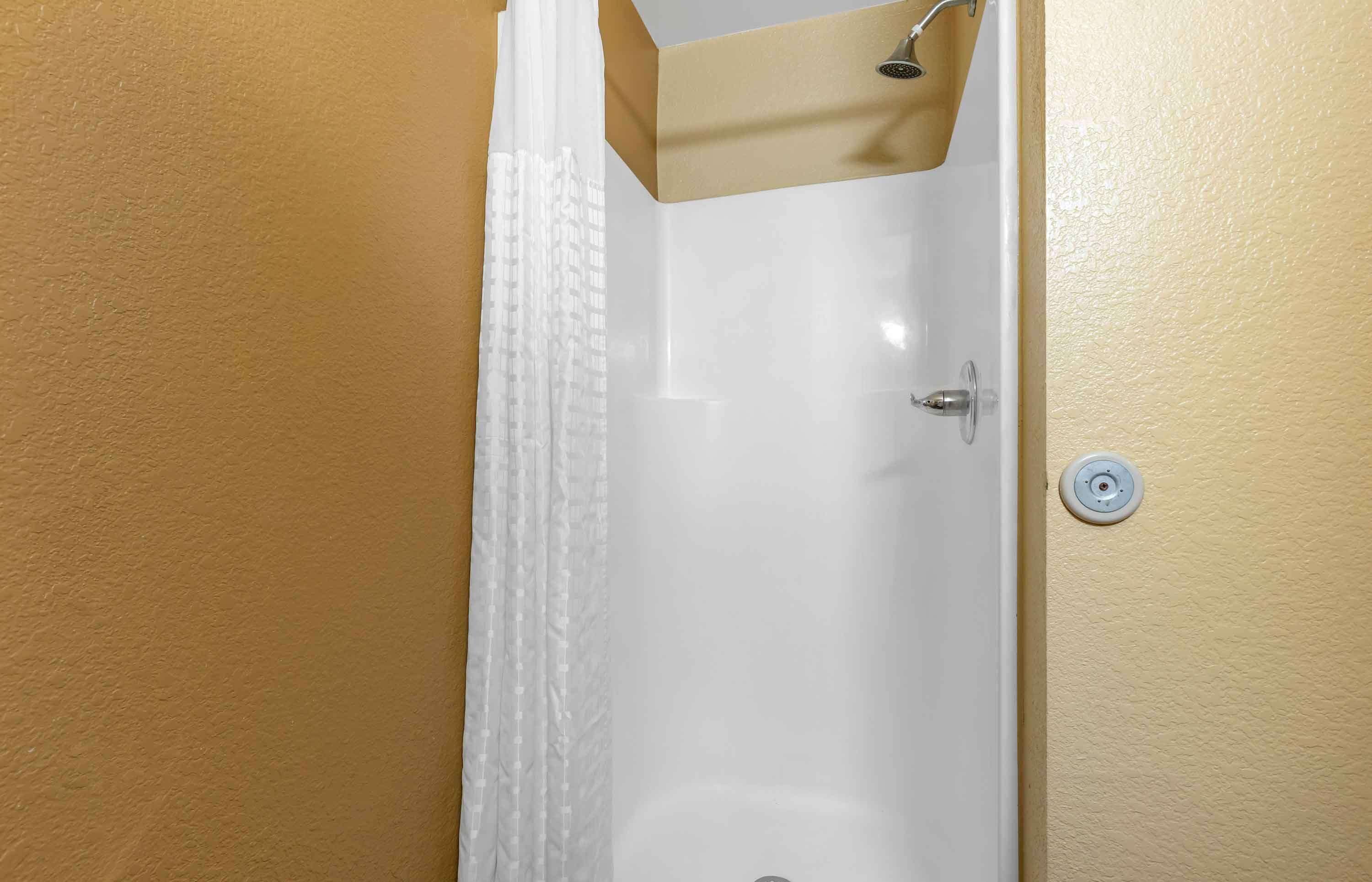 A bathroom with a white bathtub, a showerhead, and a wall-mounted control.