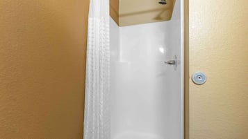 A bathroom with a white bathtub, a showerhead, and a wall-mounted control.