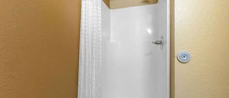 A bathroom with a white bathtub, a showerhead, and a wall-mounted control.