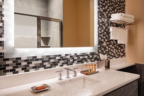 A modern bathroom with a large mirror, a sink with two faucets, a soap dish, and a towel rack with folded towels.