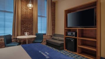 Habitación de hotel con pared de ladrillo, un televisor de pantalla plana, una mesita, dos sillas, un sofá y un minibar.