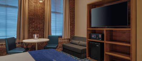 Habitación de hotel con pared de ladrillo, un televisor de pantalla plana, una mesita, dos sillas, un sofá y un minibar.