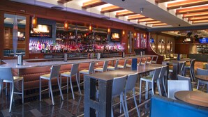 A bar area with multiple seating options including bar stools and tables, a well-stocked liquor display, and a television screen.