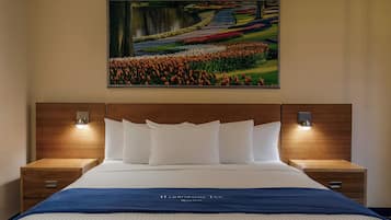 A hotel room with a large bed, two bedside tables, a headboard, and a wall-mounted painting of a garden scene.
