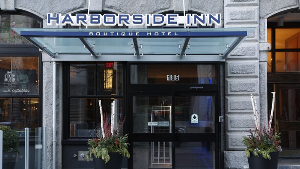 The exterior of the Harborside Inn Boutique Hotel with a glass entrance, numbered room 185, and two large potted plants at the entrance.