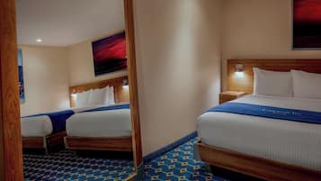 A hotel room with two beds, a mirror, a nightstand, a wall-mounted lamp, and a large painting.