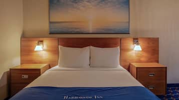 A hotel room with a bed, two bedside tables, a nightstand, a painting of a sunset over the ocean, and a blue bedspread with the hotel name.
