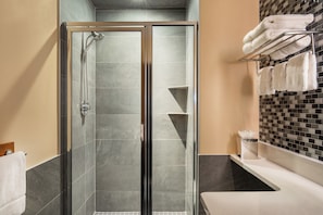 Een moderne badkamer met een douchecabine van glas, een witte wastafel en een betegelde spatwand.