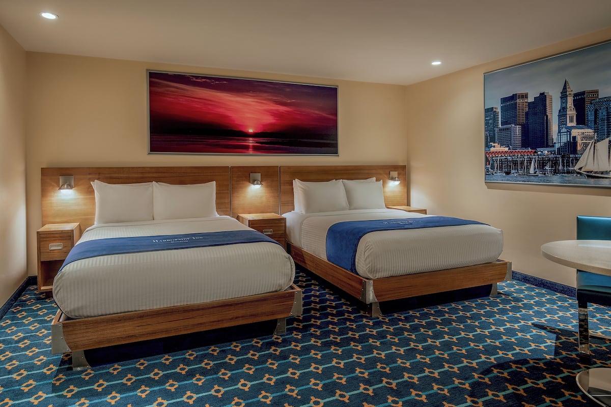 A hotel room with two beds, a cityscape painting, and a patterned carpet.